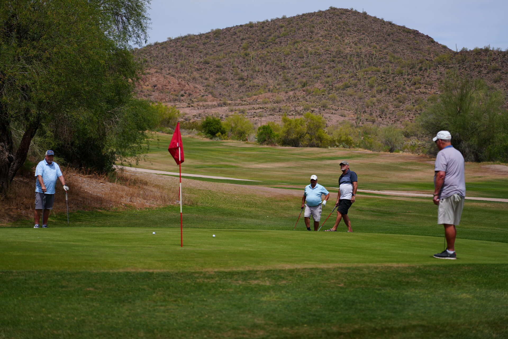 Foursome on the green of the back nine with a saguaro-covered desert hillside in the background