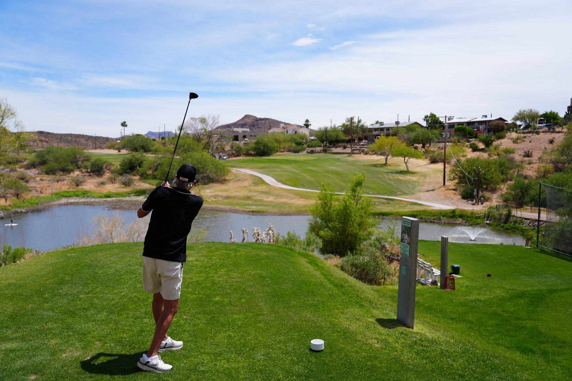 Golfer teeing off over a pond toward the Queen Valley fairway with desert mountains in the distance