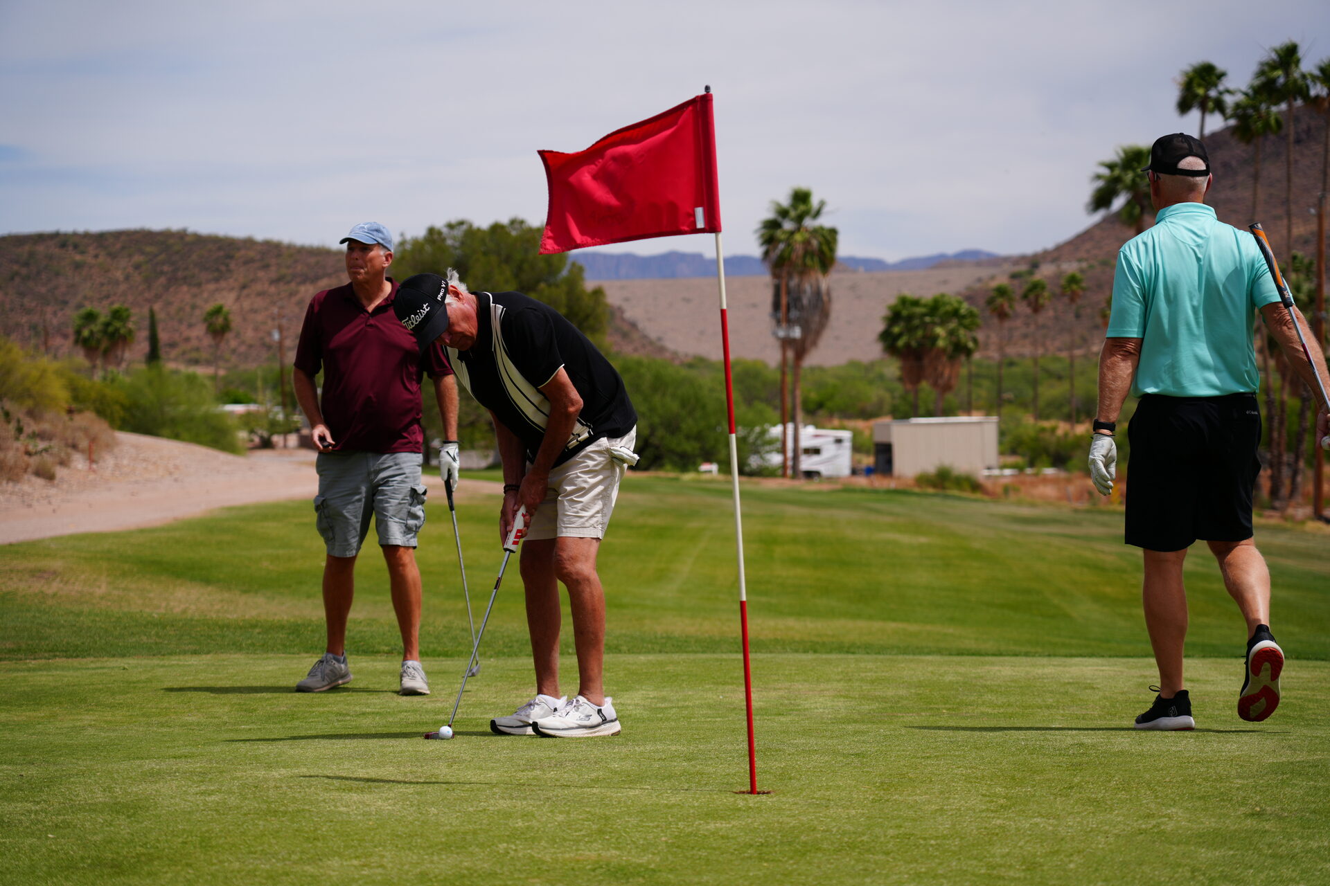 Three golfers around a flagstick on the putting green